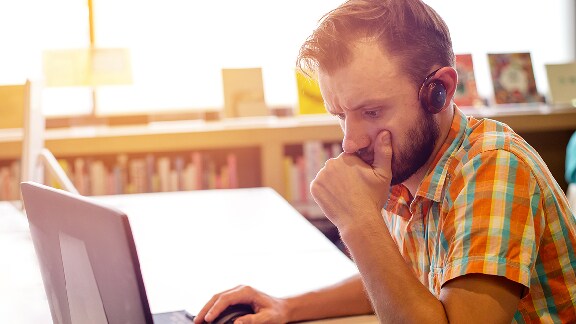 Man wearing earphones working at a laptop sitting at a table