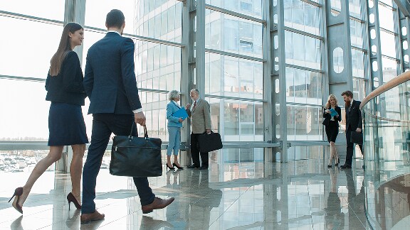 People walking in an office building hallway with full-length glass windows on one side