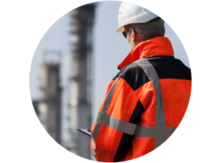 Back view of a man in a safety jacket looking towards an industrial structure in the background