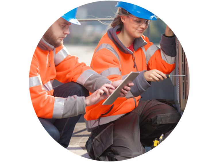 Two people in safety equipment kneeling to repair a machine