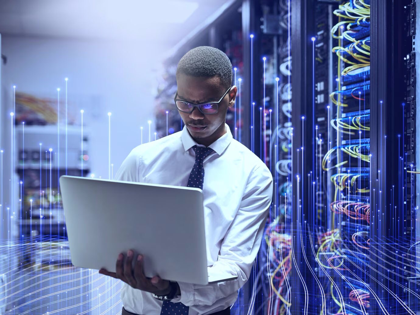 Man holding a laptop in front of a data server rack with modern graphics
